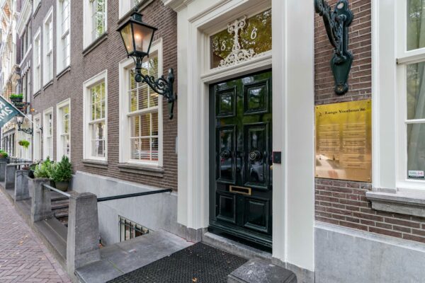 Ingang van een statig pand aan Lange Voorhout 86 met donkere voordeur, gevelverlichting en bedrijfsnaamplaat.